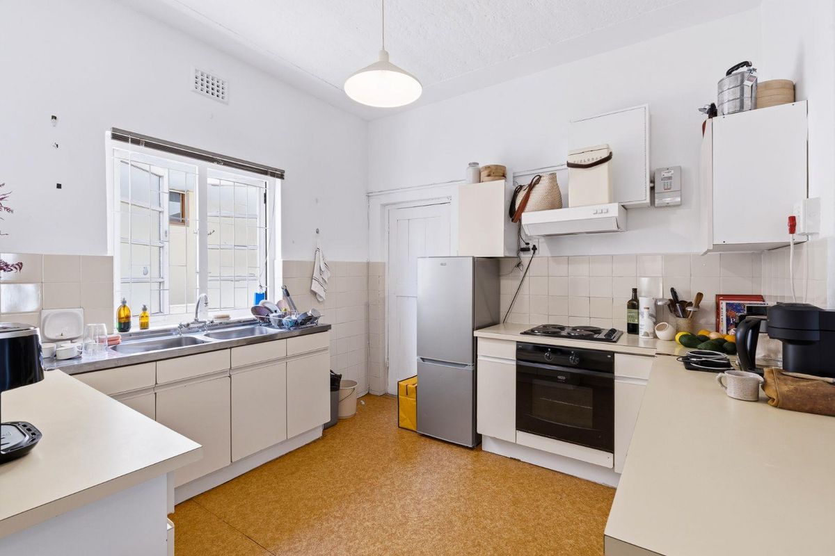 A functional kitchen featuring built-in cabinetry, a stainless steel double sink, electric cooktop, and oven, with a tiled splashback and original flooring.
