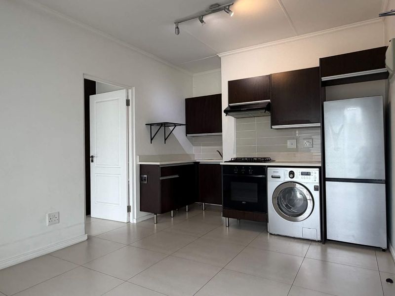 A clean, functional kitchen featuring dark cabinetry, built-in oven and hob, extractor fan, and neutral tiled flooring in an open-plan layout.