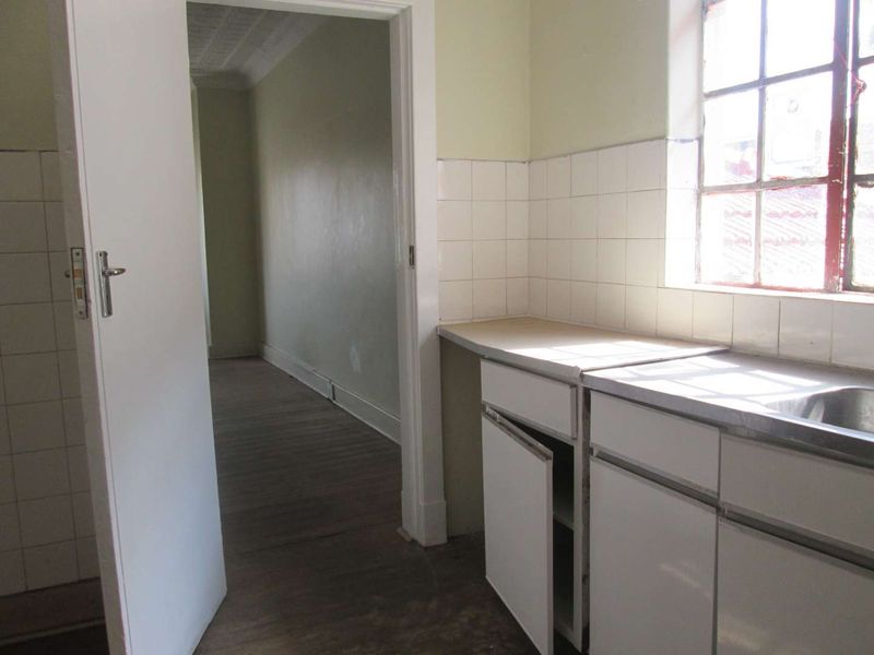 A dated kitchen area featuring basic built-in cabinetry, a stainless steel sink, and tiled splashbacks, requiring renovation to modernize the space.