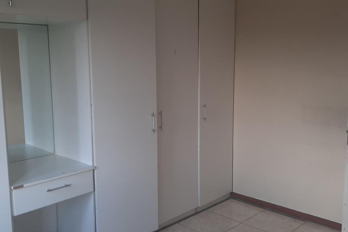 A functional bedroom featuring built-in cupboards and a vanity unit with tiled flooring, offering a clean and neutral space ready for personalization.
