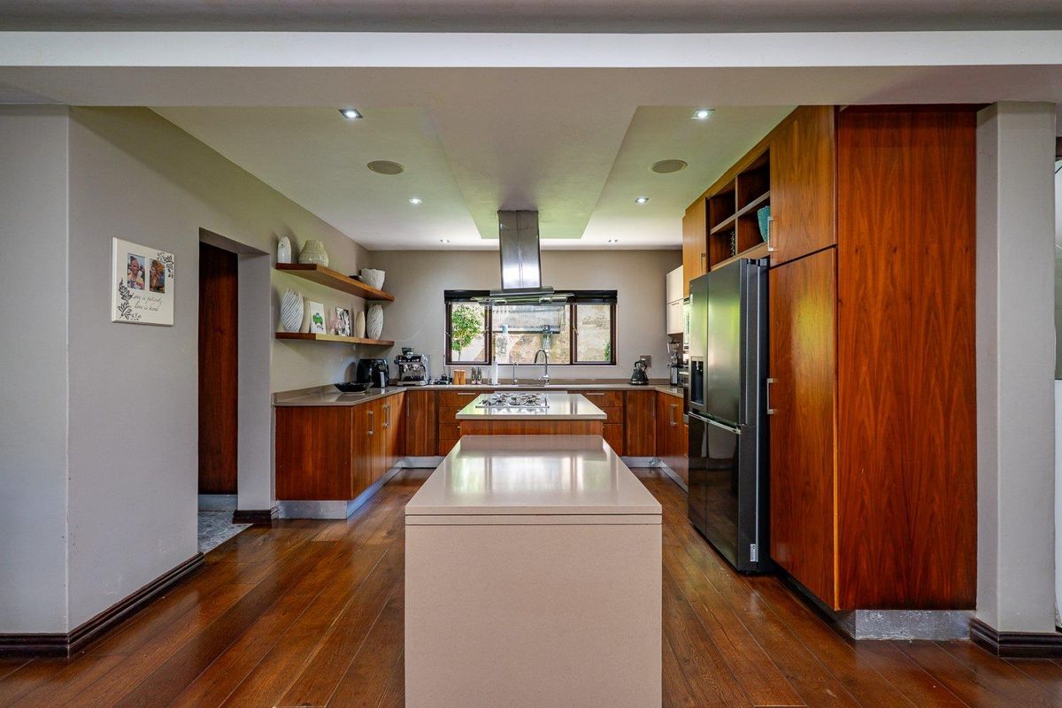 A modern kitchen featuring warm wood cabinetry, stone countertops, a central island, and integrated stainless steel appliances with recessed ceiling lighting.