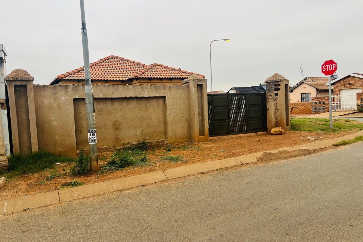 Front view of the property featuring a perimeter wall, metal gate, and tiled roof structure.
