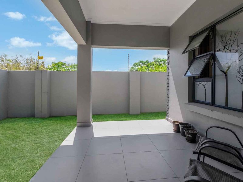 A covered patio area featuring tiled flooring, overlooking a private garden enclosed by high perimeter walls with electric fencing.