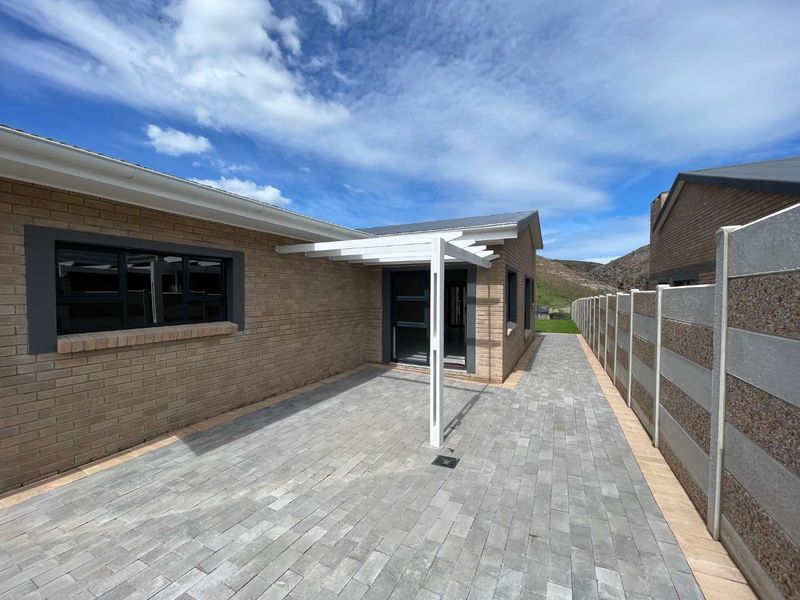 A well-maintained rear exterior featuring a paved patio area, a modern pergola, and a secure precast concrete boundary wall.