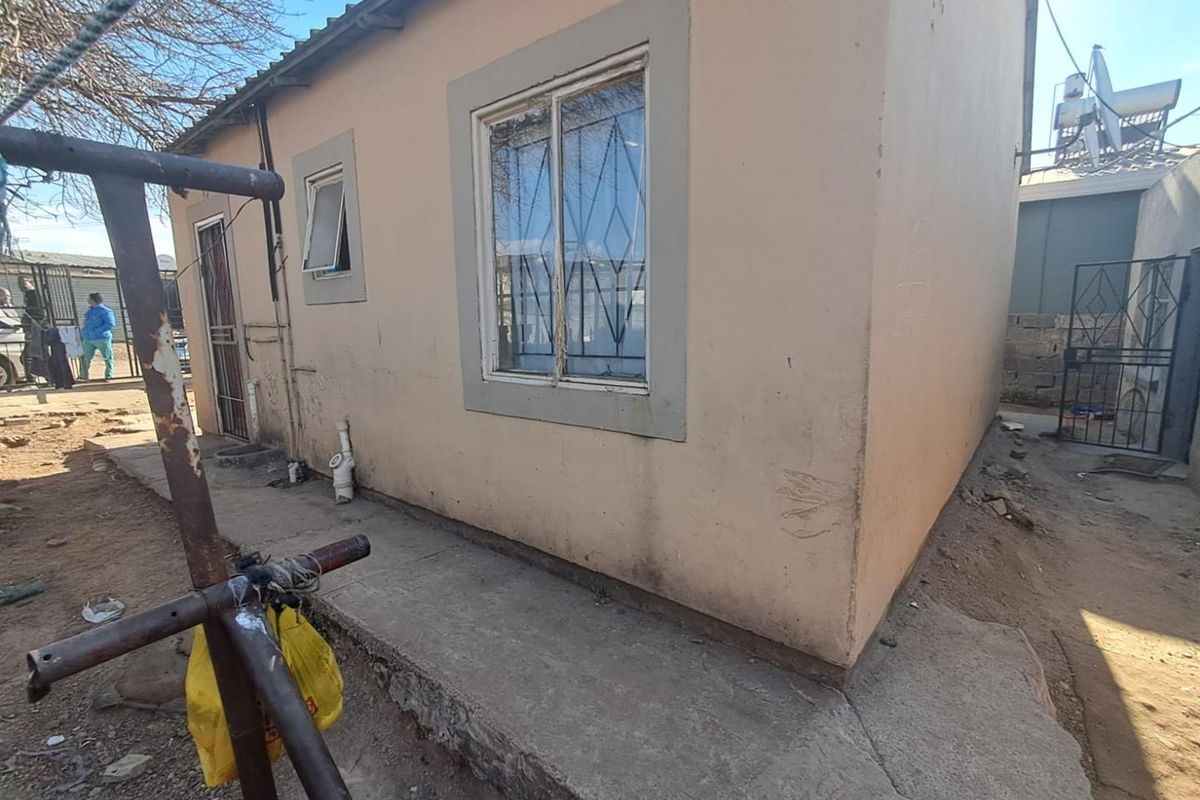 Rear exterior view of the property showing a concrete apron, security bars on windows, and basic masonry wall finish.