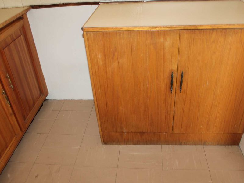 A dated kitchen area featuring wooden cabinetry, laminate countertops, and tiled flooring, presenting an opportunity for modernization and renovation.