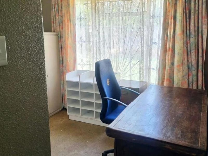 A small home office space featuring a large window with security bars and neutral wall finishes.
