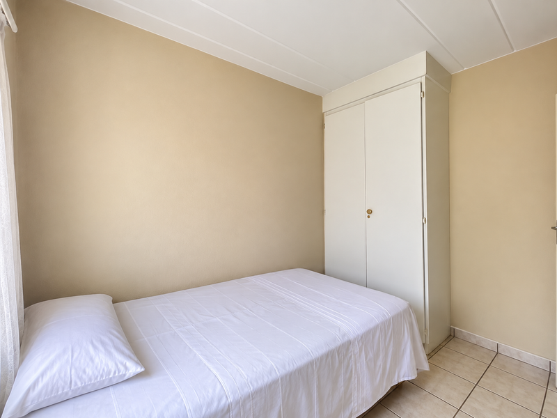 A simple bedroom featuring neutral wall tones, tiled flooring, and a functional built-in wardrobe.