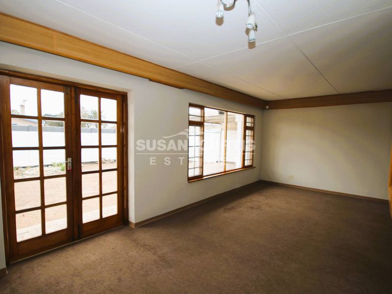 Spacious living room featuring carpeted flooring, timber-framed windows, and wooden French doors providing direct access to the outdoor area.