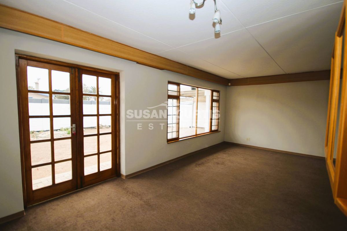 Spacious living room featuring carpeted flooring, timber-framed windows, and wooden French doors providing direct access to the outdoor area.
