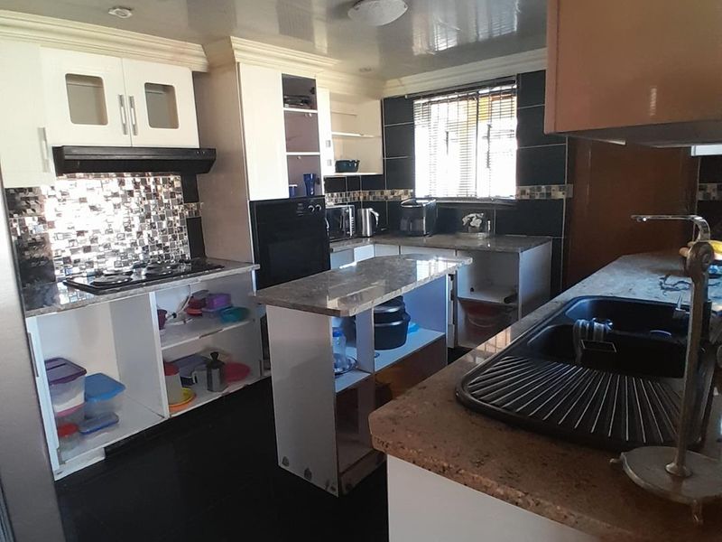 A functional kitchen featuring granite countertops, built-in cabinetry, and a central island, though it requires some cosmetic updates to cabinet doors and finishes.