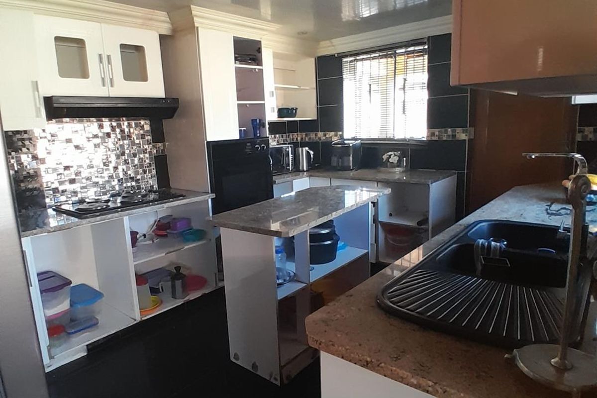 A functional kitchen featuring granite countertops, built-in cabinetry, and a central island, though it requires some cosmetic updates to cabinet doors and finishes.