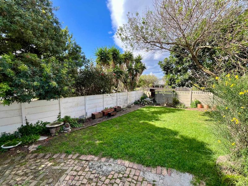 A private rear garden featuring a lawn area, established trees, and a brick-paved patio enclosed by precast concrete boundary walls.
