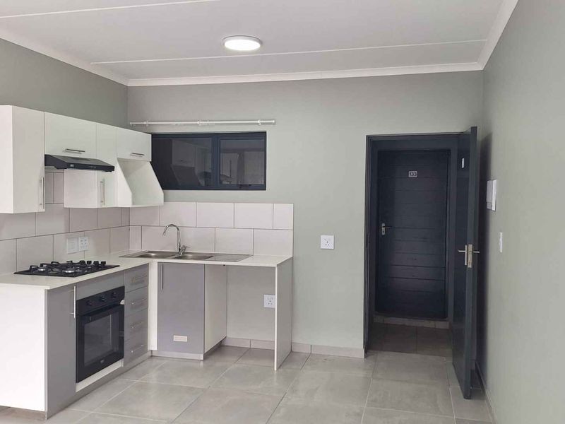 A clean, modern kitchen featuring built-in cabinetry, a gas hob, electric oven, extractor fan, and tiled finishes in a neutral color palette.