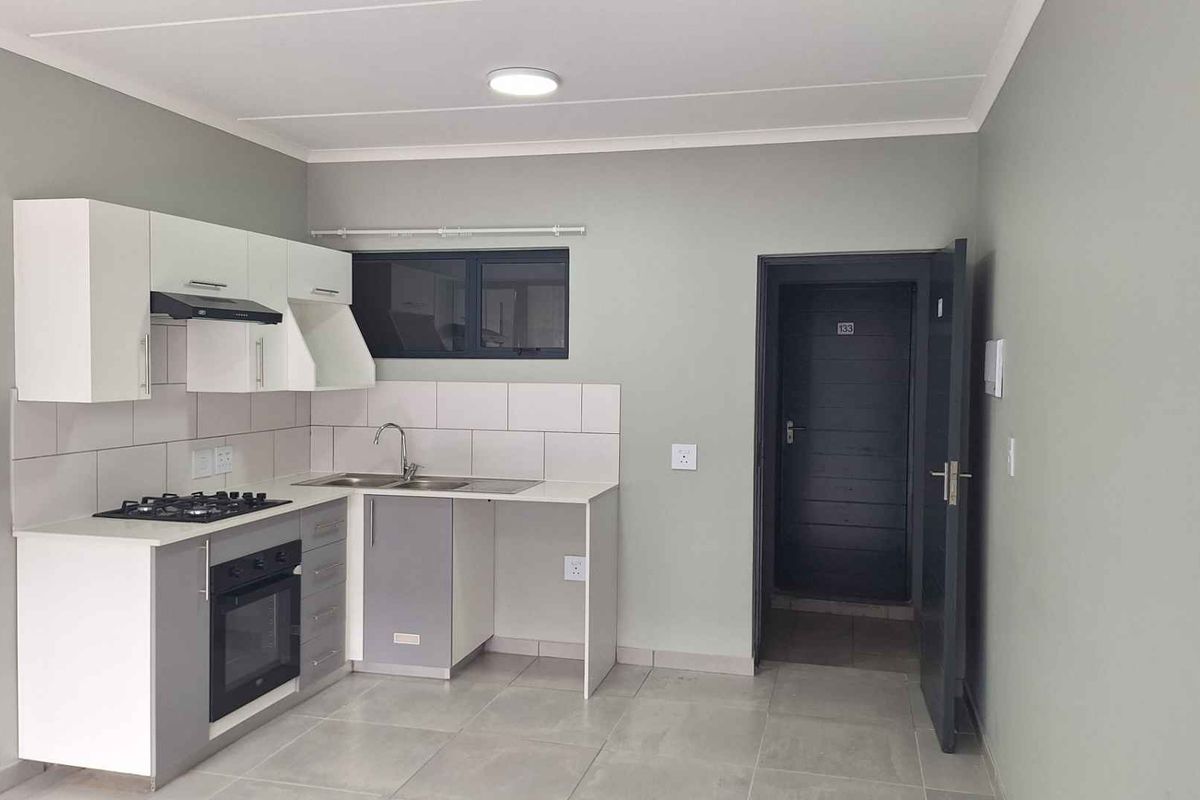 A clean, modern kitchen featuring built-in cabinetry, a gas hob, electric oven, extractor fan, and tiled finishes in a neutral color palette.