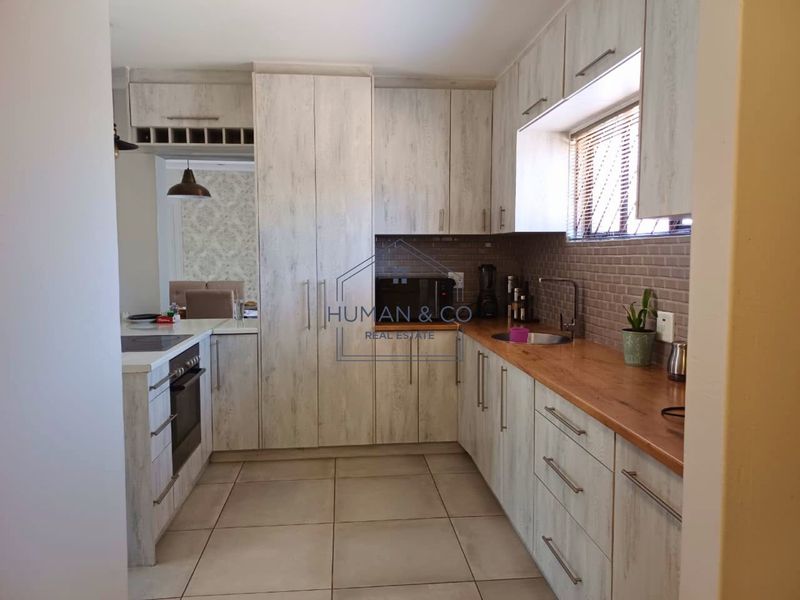 A functional kitchen featuring light wood-grain cabinetry, wooden countertops, tiled flooring, and integrated appliances including an oven and hob.