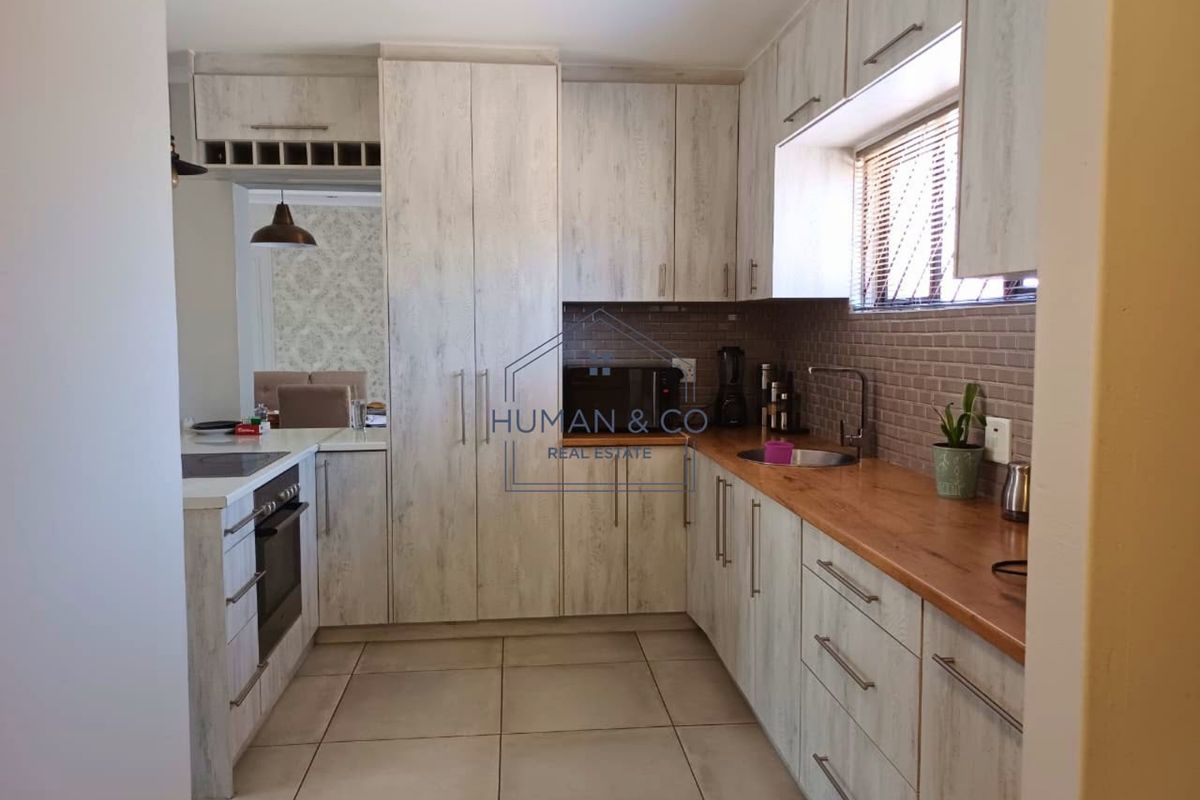 A functional kitchen featuring light wood-grain cabinetry, wooden countertops, tiled flooring, and integrated appliances including an oven and hob.