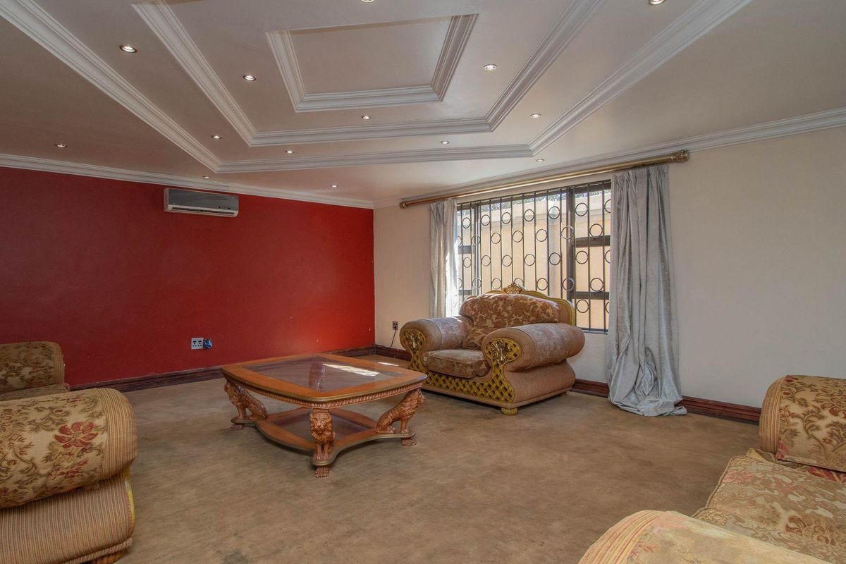 Spacious living room featuring a decorative tray ceiling with recessed lighting, wall-mounted air conditioning unit, and security bars on the window.