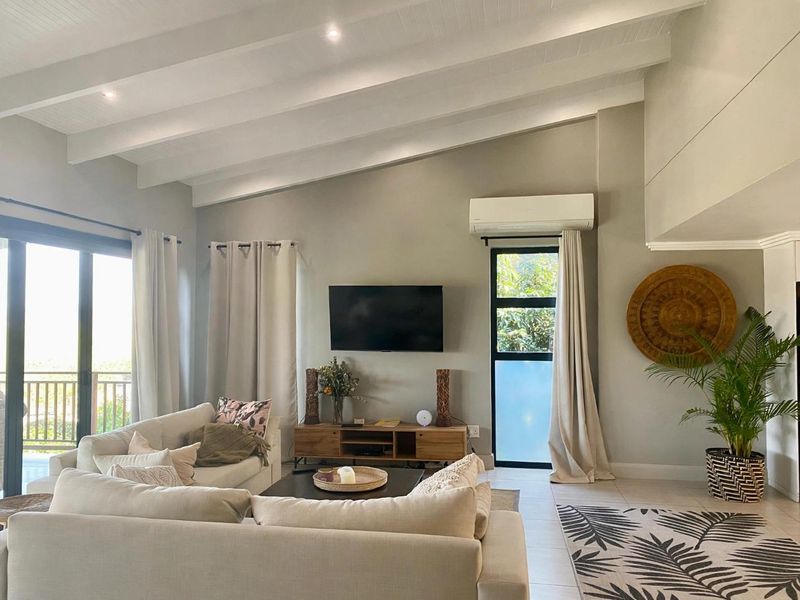 Spacious living room featuring a high vaulted ceiling with exposed beams, tiled flooring, and large sliding glass doors leading to an outdoor area.