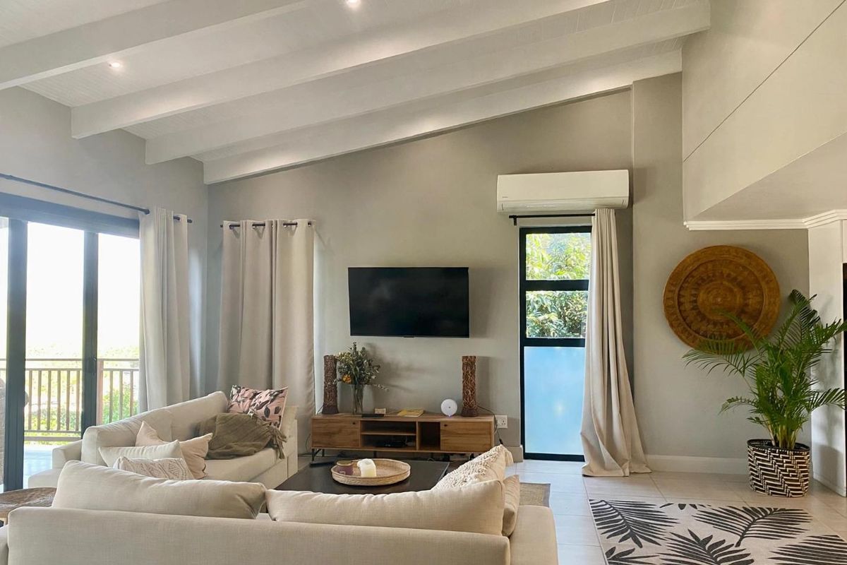 Spacious living room featuring a high vaulted ceiling with exposed beams, tiled flooring, and large sliding glass doors leading to an outdoor area.