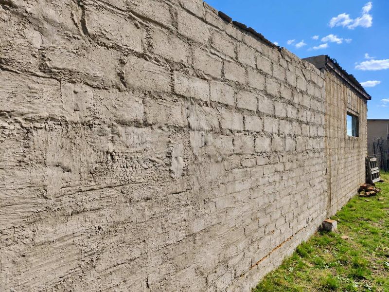 An exterior view of a farm building featuring an unfinished concrete block wall with a rough cement render finish.
