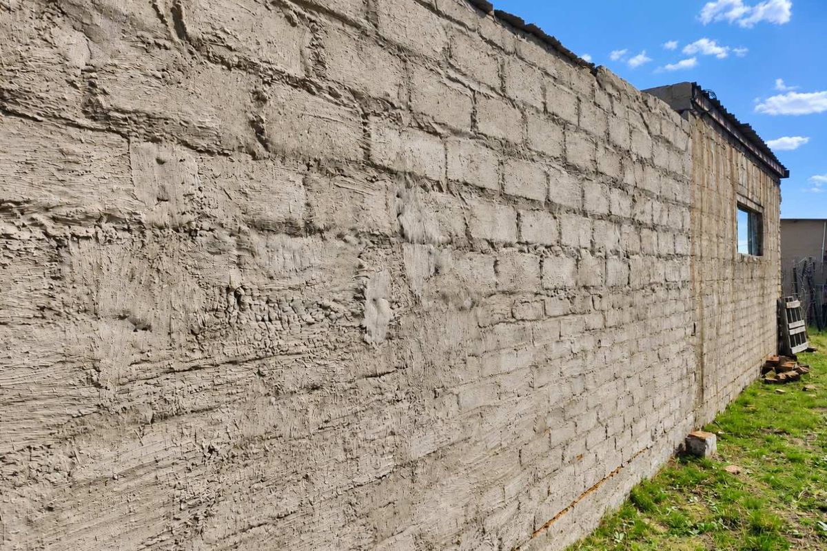 An exterior view of a farm building featuring an unfinished concrete block wall with a rough cement render finish.