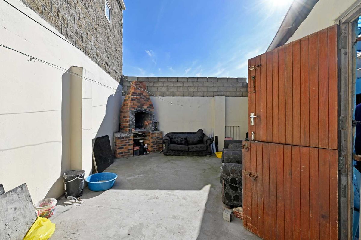 Rear courtyard area featuring a built-in brick braai, concrete paving, and a timber stable door, enclosed by boundary walls.
