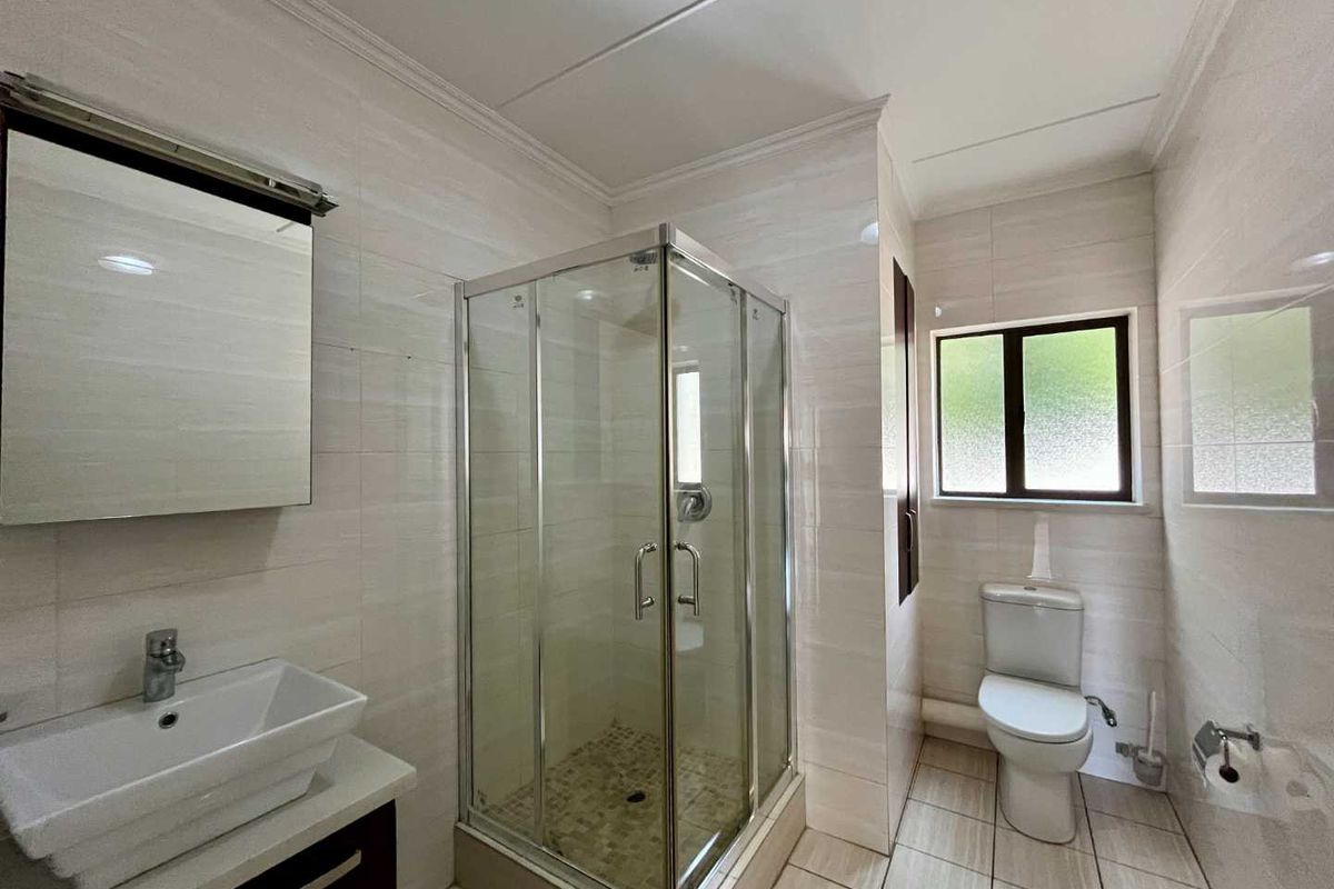 A modern bathroom featuring a glass-enclosed shower, a vanity with a vessel sink, and a toilet, finished with neutral wall and floor tiles.