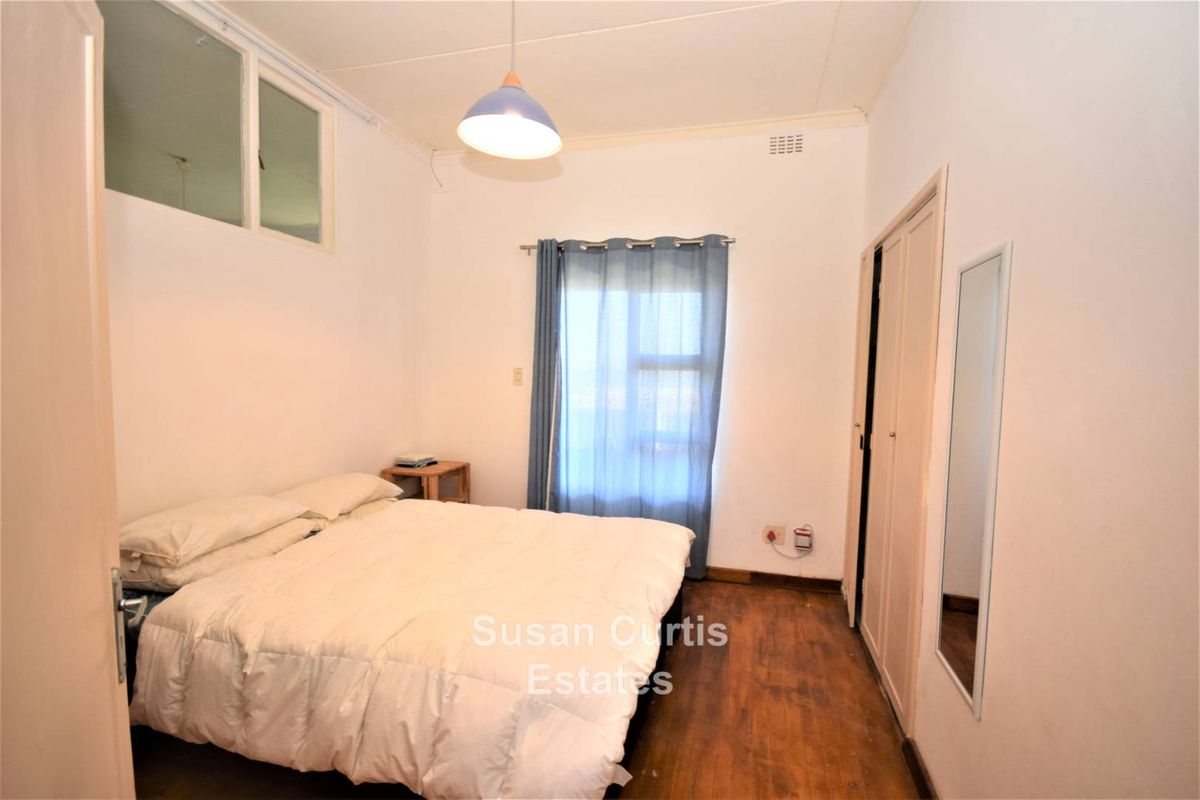 A functional bedroom featuring built-in cupboards, timber flooring, and a high-level window providing natural light.