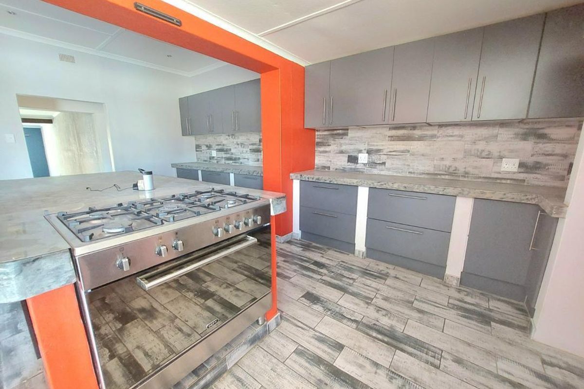 Modern kitchen featuring grey built-in cabinetry, stone countertops, a gas stove with oven, and wood-look tiled flooring with a bold orange accent wall.