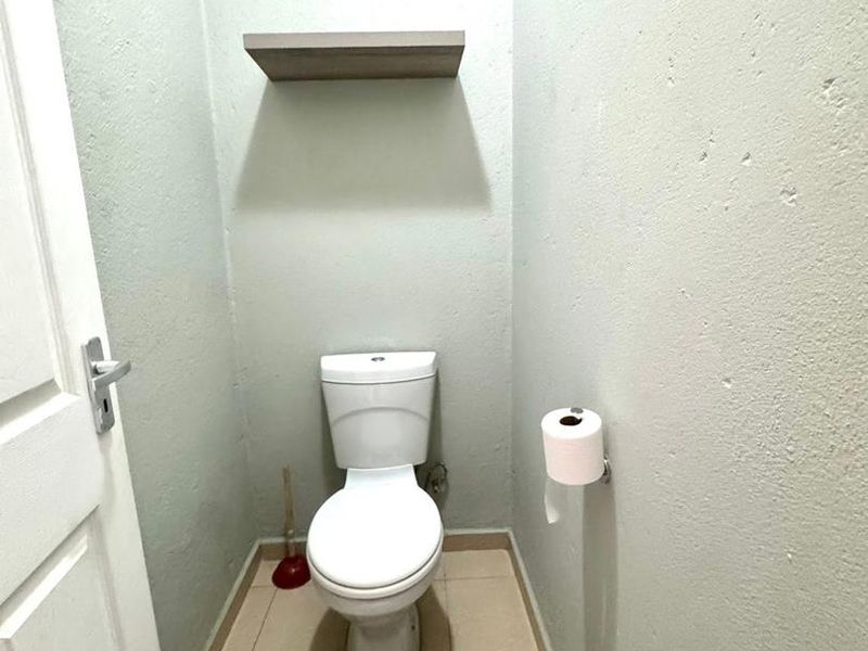 A compact guest bathroom featuring a standard toilet, tiled flooring, and a wall-mounted floating shelf.