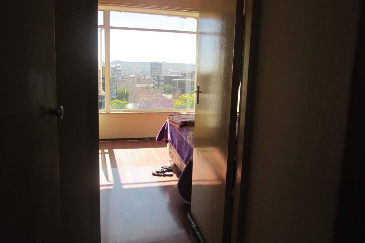 A view into a bedroom featuring large windows with natural light and urban views, finished with wood-look flooring.