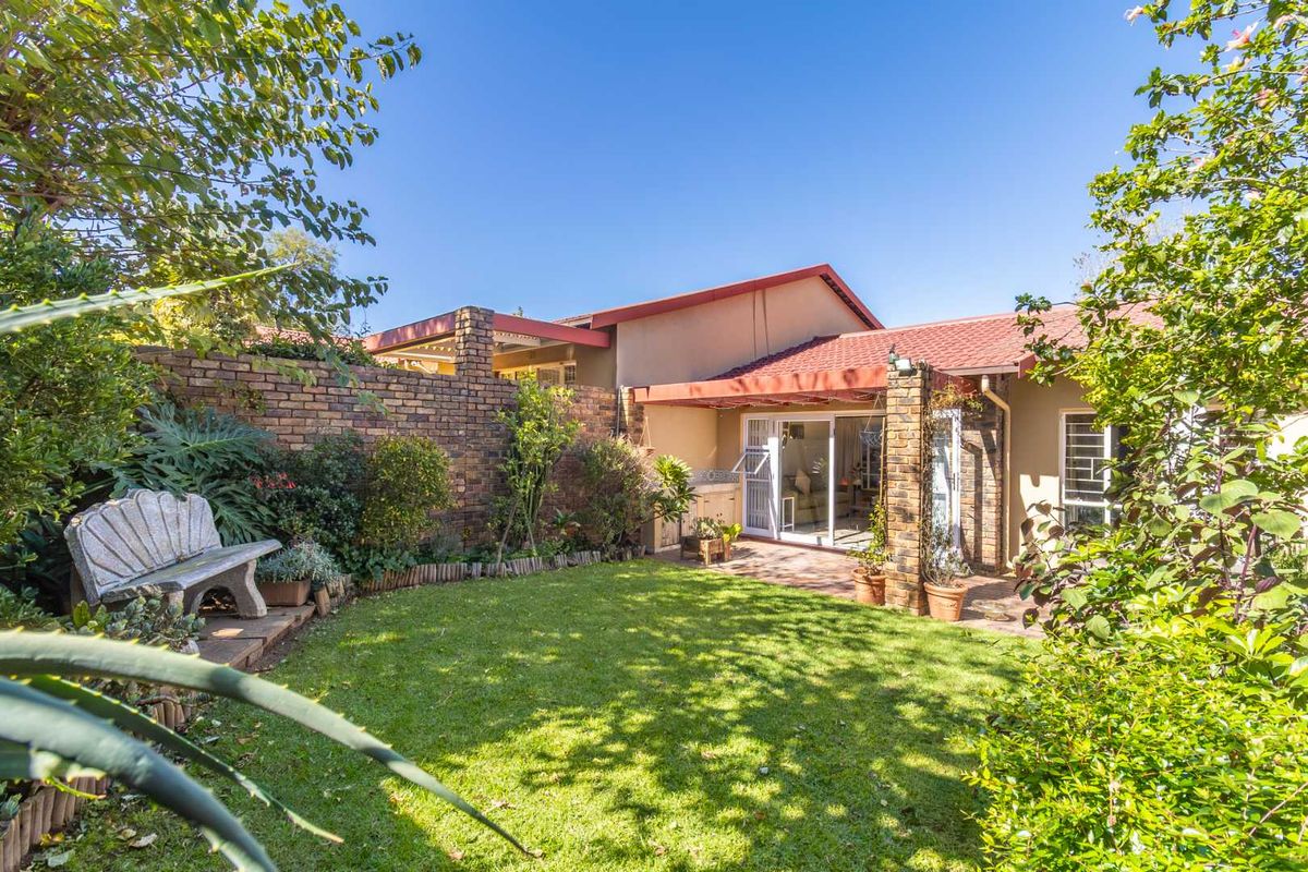 A private rear garden featuring a lawn, established landscaping, a brick boundary wall, and a covered patio area with sliding door access to the home.
