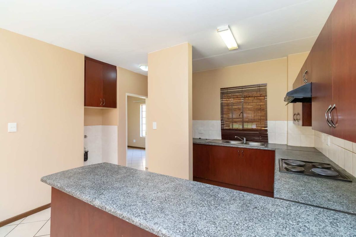 Functional kitchen featuring dark wood cabinetry, granite countertops, built-in electric hob with extractor fan, and tiled backsplash, offering a clean and practical workspace.