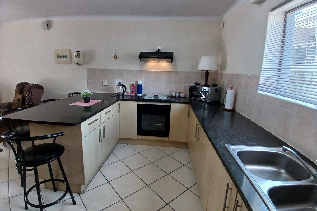 A functional kitchen featuring granite countertops, built-in oven, extractor fan, double bowl stainless steel sink, and light-toned cabinetry with tiled flooring.