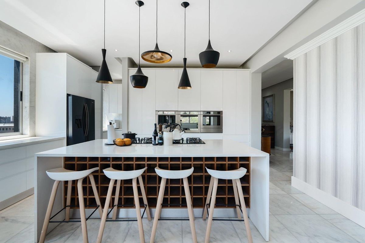 Modern kitchen featuring a large central island with integrated wine storage, high-end built-in appliances, sleek handleless cabinetry, and elegant marble flooring.