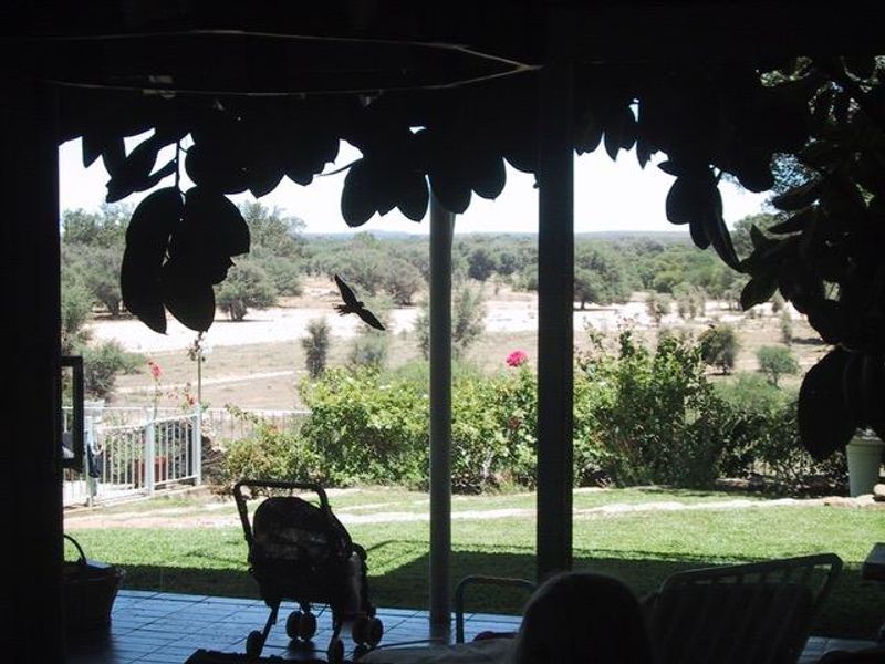 A covered patio area featuring tiled flooring and support columns, offering an open view of the surrounding landscape and garden.