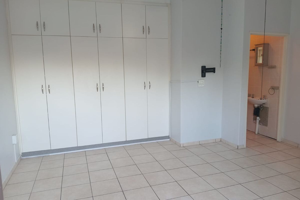 A spacious bedroom featuring extensive built-in cupboards, neutral tiled flooring, and direct access to an en-suite bathroom.