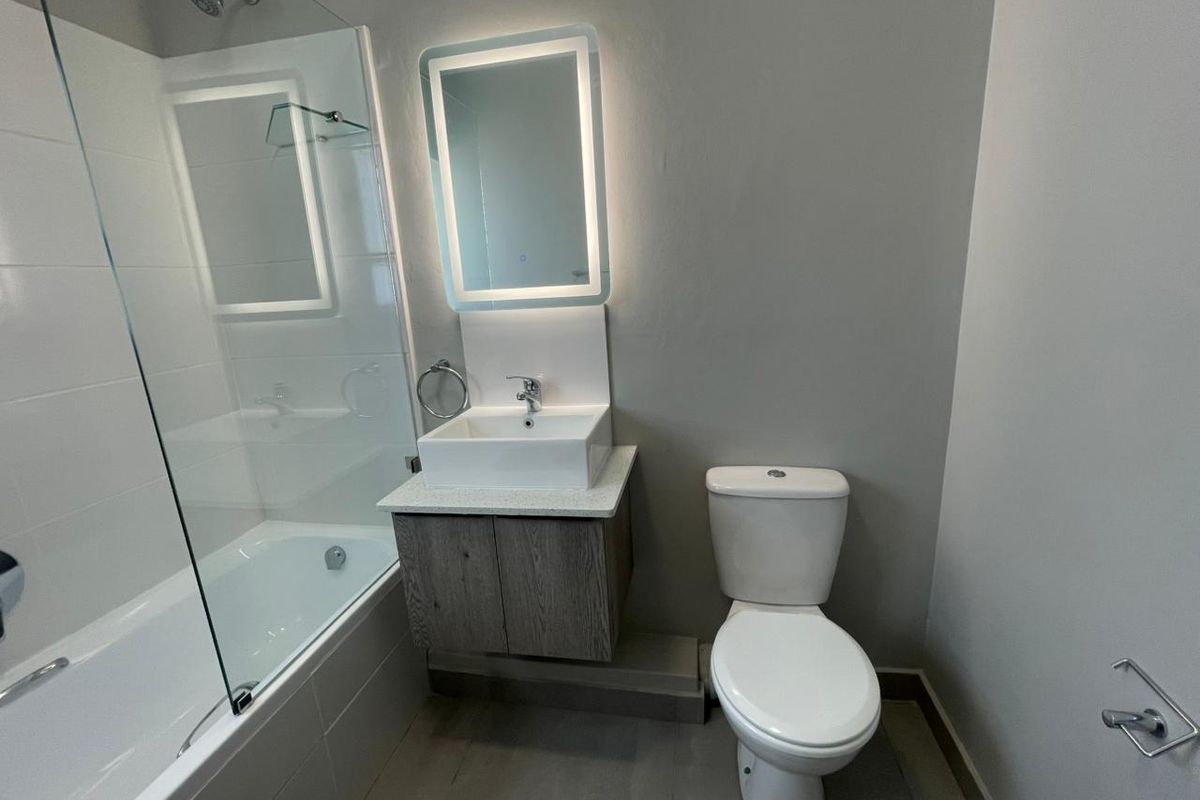 Modern bathroom featuring a glass-enclosed shower over the bathtub, a floating vanity with a vessel sink, and an illuminated wall mirror.
