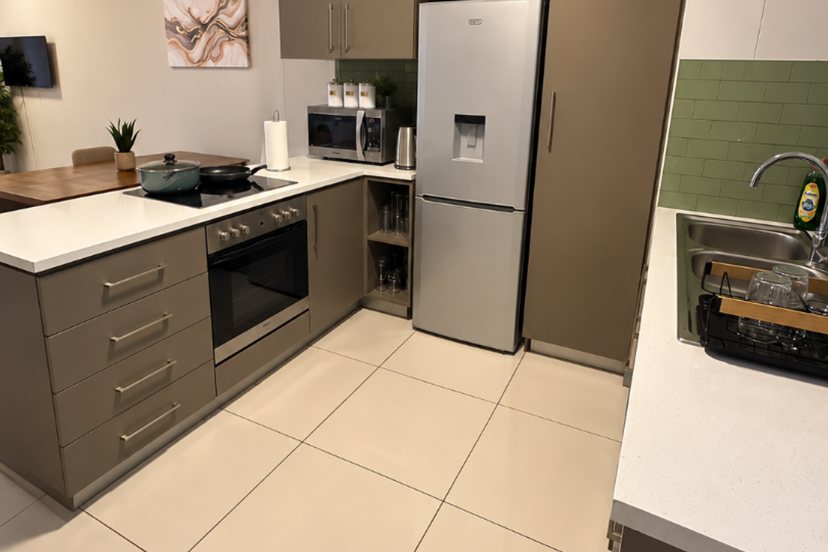 Modern kitchen featuring sleek taupe cabinetry, white stone countertops, a tiled backsplash, and integrated appliances, seamlessly flowing into the adjacent living area.