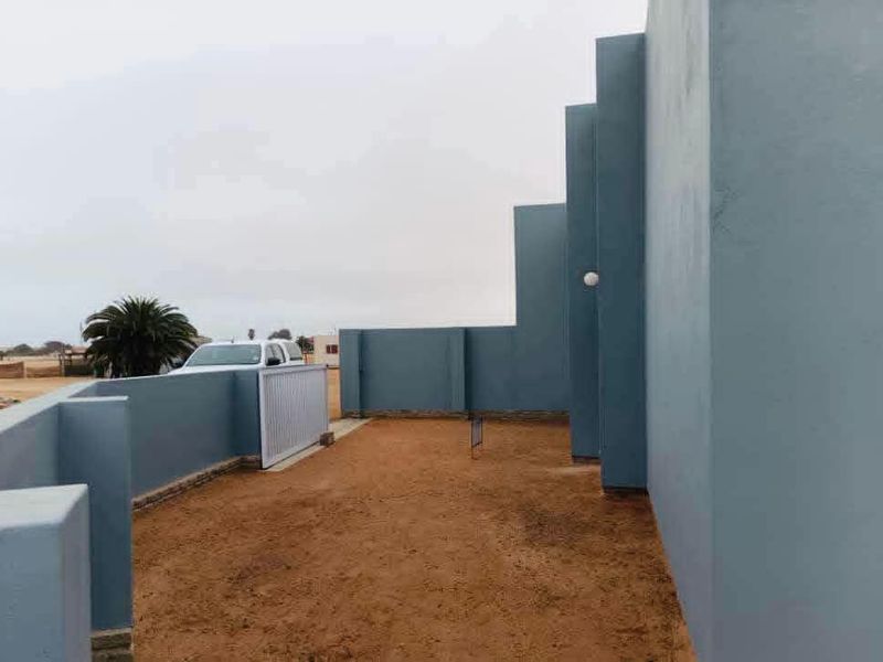 A view of the rear exterior area featuring a boundary wall, sliding gate, and exterior wall lighting.