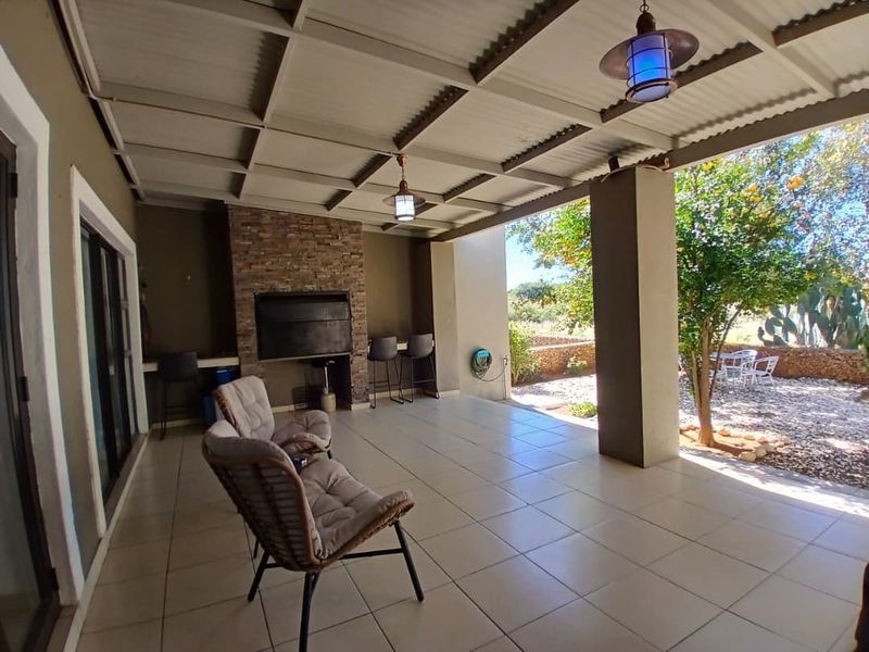 Spacious covered patio featuring a built-in braai with stone cladding, tiled flooring, and direct access to the garden area.