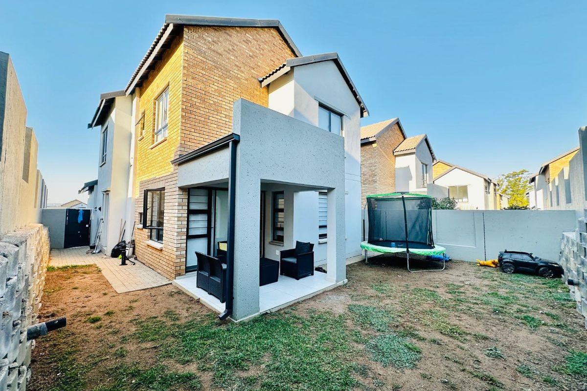 Rear view of the cluster home featuring a covered patio, brick and plaster facade, and a private garden area with boundary walls.