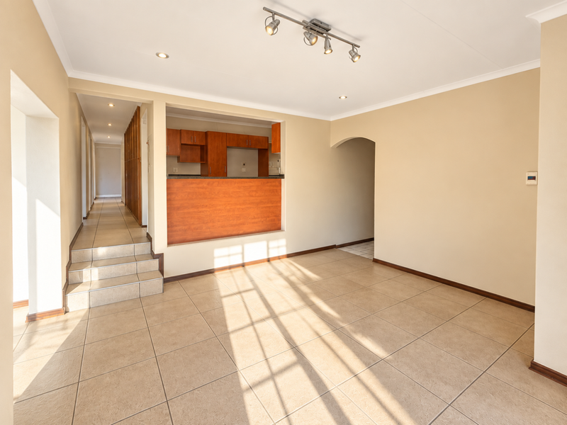 Spacious open-plan living area featuring tiled floors, a kitchen pass-through window, and a tiled staircase leading to a hallway.