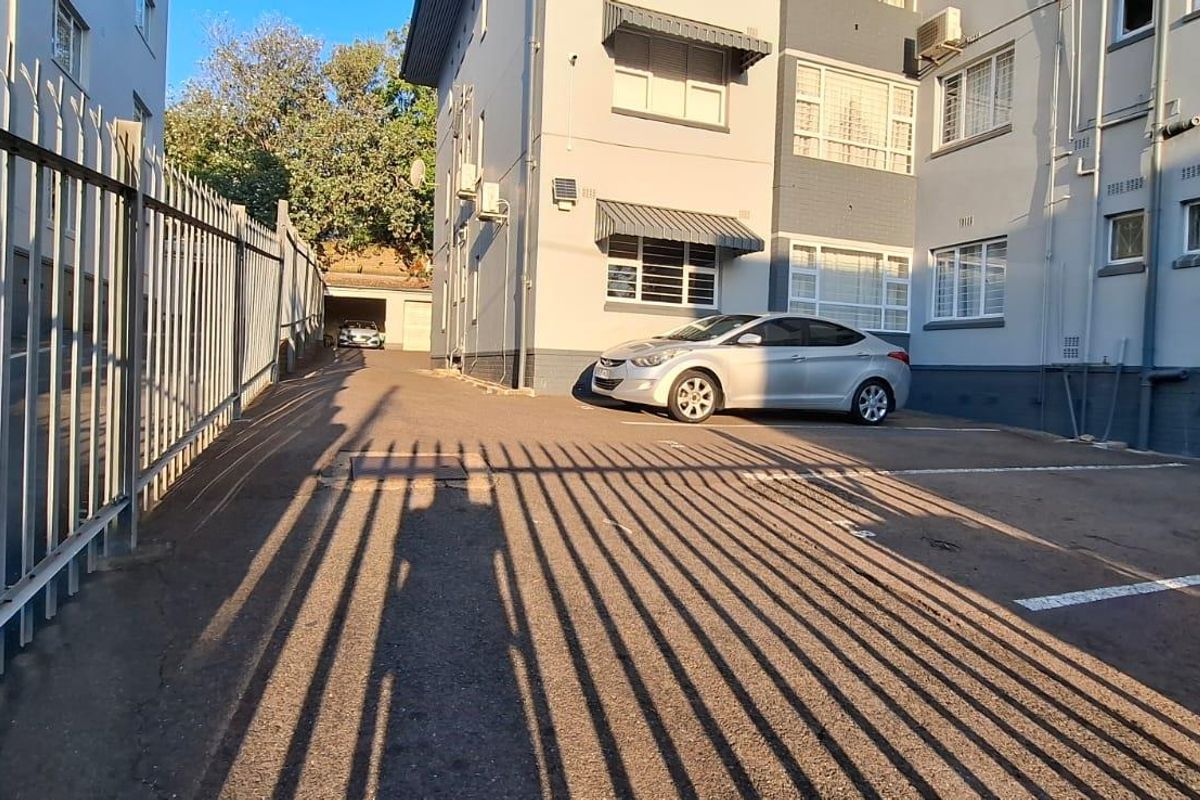 Exterior view of the apartment building showing the paved parking area, security fencing, and building facade with window security bars.