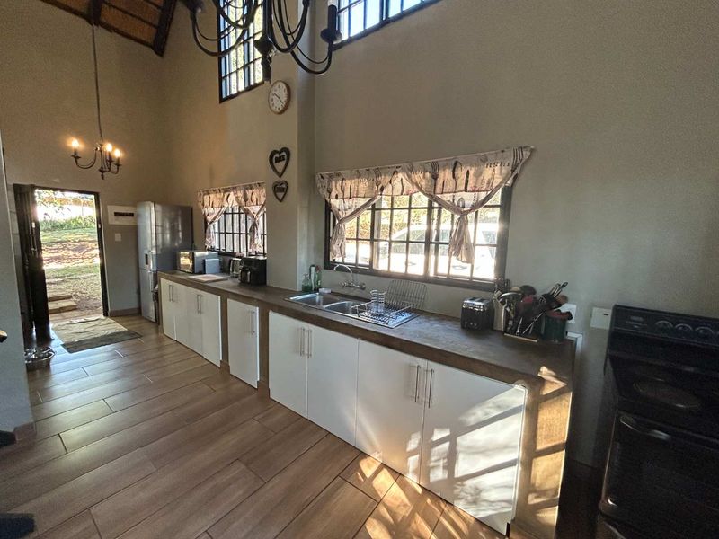 Spacious kitchen featuring vaulted ceilings with exposed rafters, modern white cabinetry, wood-look tiled flooring, and ample natural light from large windows.