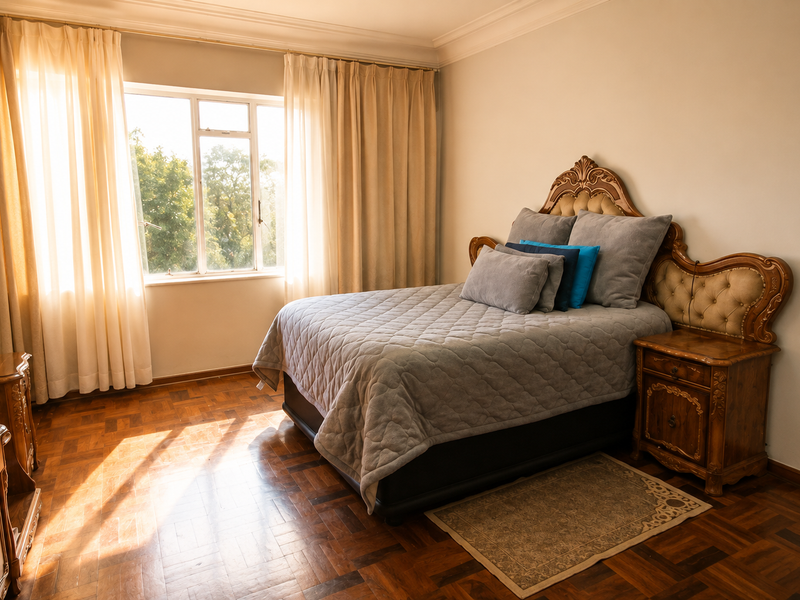 A well-lit bedroom featuring classic parquet flooring, decorative cornice detailing, and a large window allowing for ample natural light.