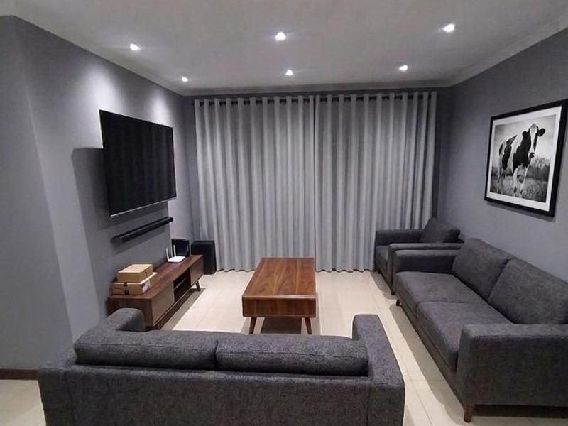 A modern living room featuring neutral grey walls, tiled flooring, and recessed downlighting, creating a clean and contemporary atmosphere.