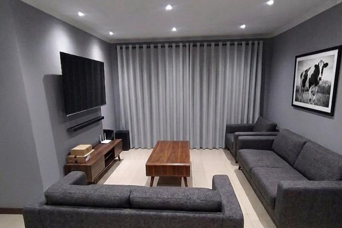 A modern living room featuring neutral grey walls, tiled flooring, and recessed downlighting, creating a clean and contemporary atmosphere.