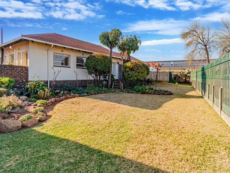 A well-maintained rear garden featuring a paved walkway, established garden beds, and secure perimeter fencing surrounding the property.